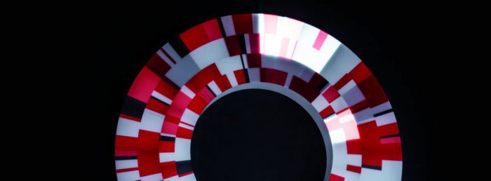 Das Bild zeigt einen irisförmigen Ring aus pixelartig zusammengesetzten Farbeckchen in Rot-, Schwarz- und Grautönen auf tiefschwarzem Untergrund.