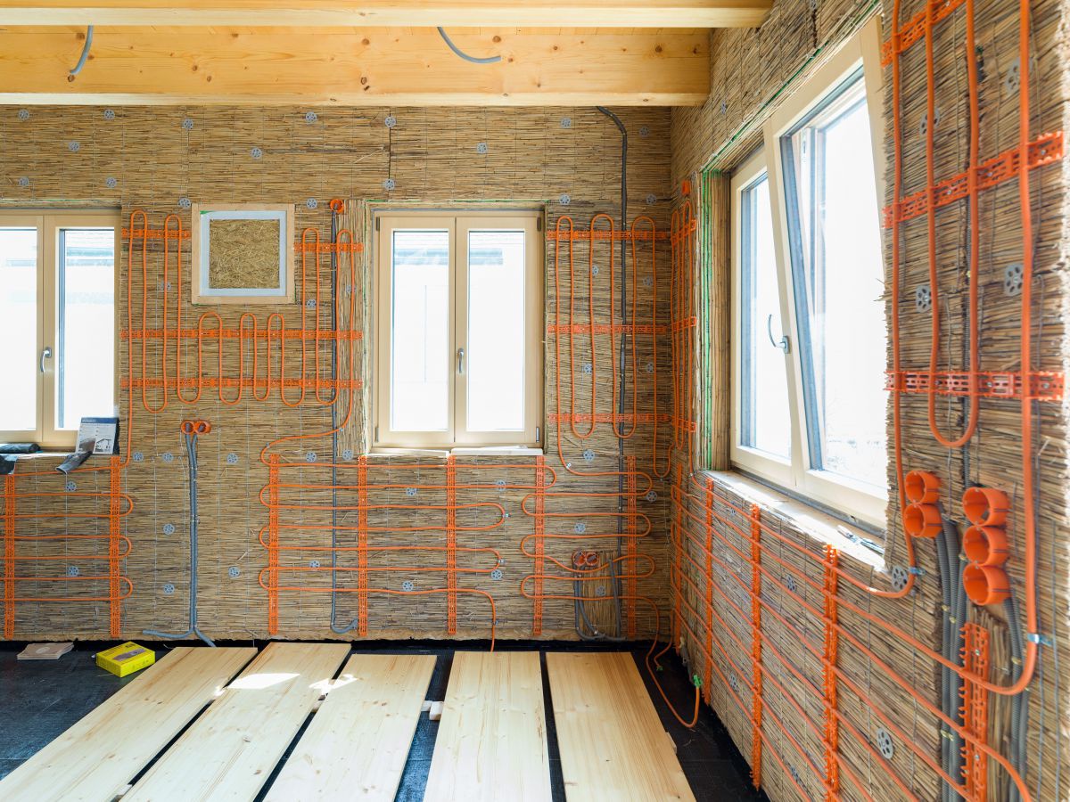 Das Haus von innen: Holzwände mit Stroh gedämmt, die Fenster sind schon drin. Die Wandheizung besteht aus orangefarbenen Schläuchen. Am Boden liegen breite Holzlatten auf einer schwarzen Isolierung.