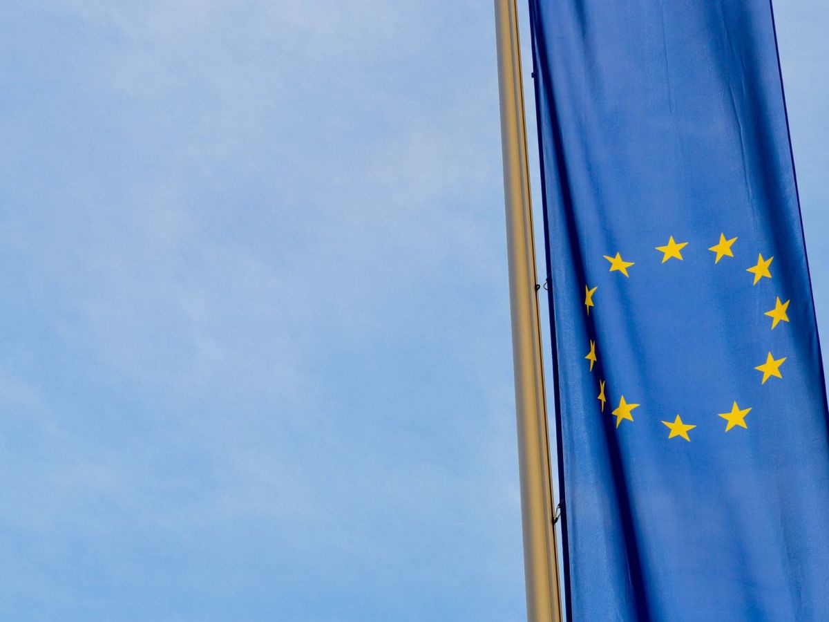 Die Flagge der Europäischen Union (ein Kreis aus 12 gelben Sternen auf tiefblauem Grund) an einem Fahnenmasten vor blauem Himmel.