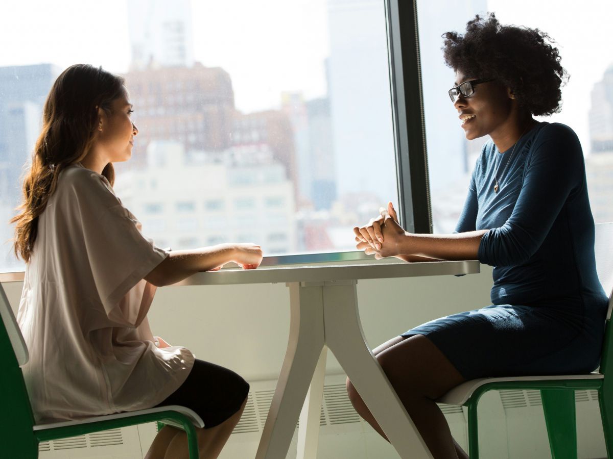 Zwei Frauen sitzen sich gegenüber an einem runden Tisch und sind sichtbar in ein wichtiges Gespräch vertieft.