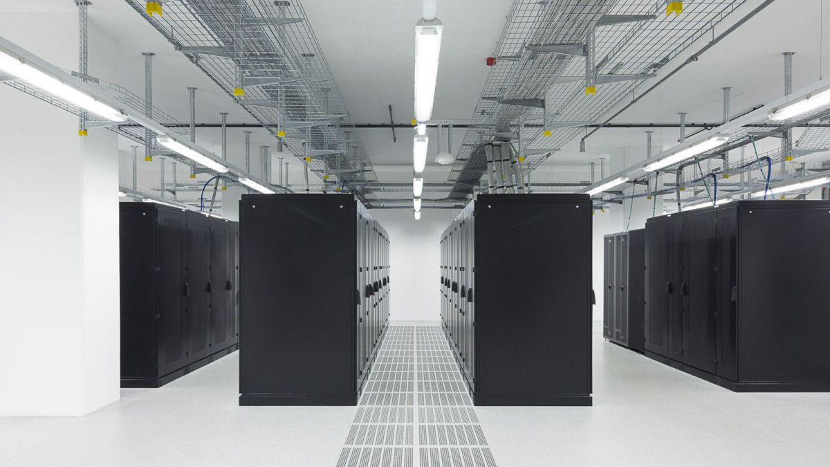 Blick in den Serverraum des Rechenzentrums der Stadt Wien: Schwarze Kästen in langen Reihen, sonst ist der Raum kahl und weiß, Neonröhren an der Decke, Lüftungsgitter und Kabelkanäle.