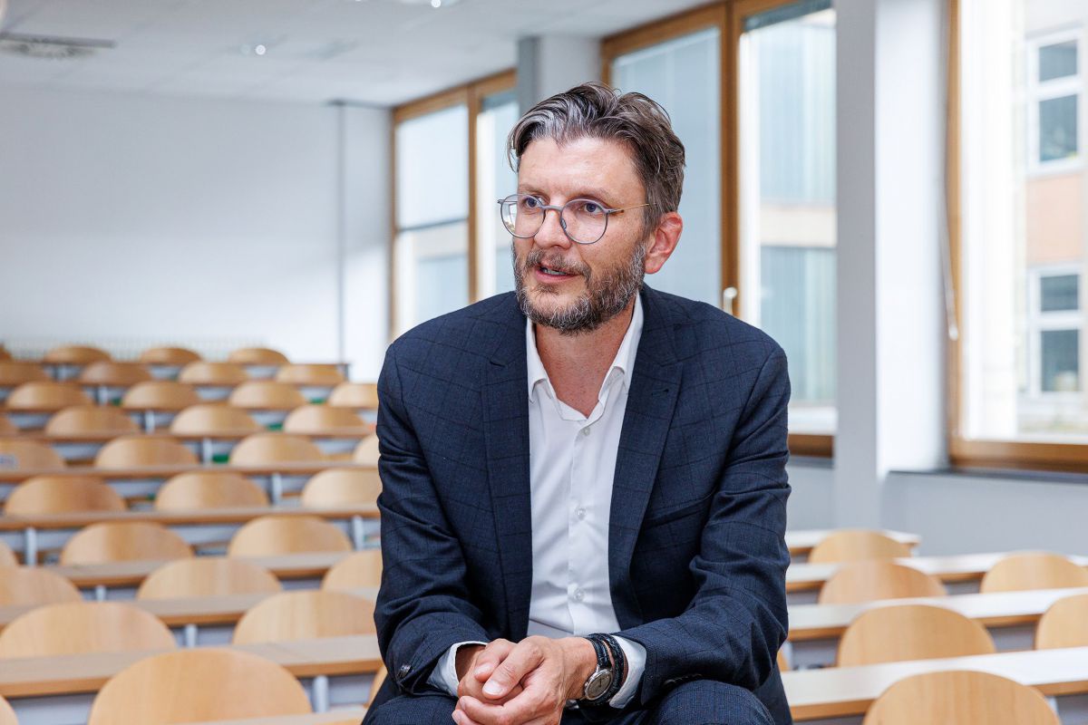 Univ.-Prof. DI. Dr. Thomas Kienberger von der Montanuniversität Leoben sitzt vor den leeren Stühlen in einem Hörsaal. Er trägt Vollbart, eine runde Brille, Kopfhaar und Bart sind grau meliert. Über weißem Hemd mit offenem Kragen trägt er ein dunkelblaues 