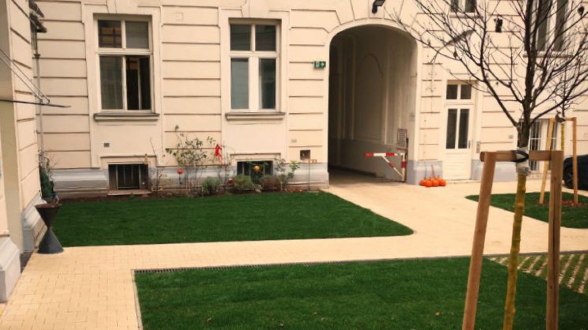 In einem Wiener Innenhof wurde der Boden teilweise entsiegelt und begrünt, in den Ecken sind jetzt Rasenflächen statt Beton und auch junge Bäume.