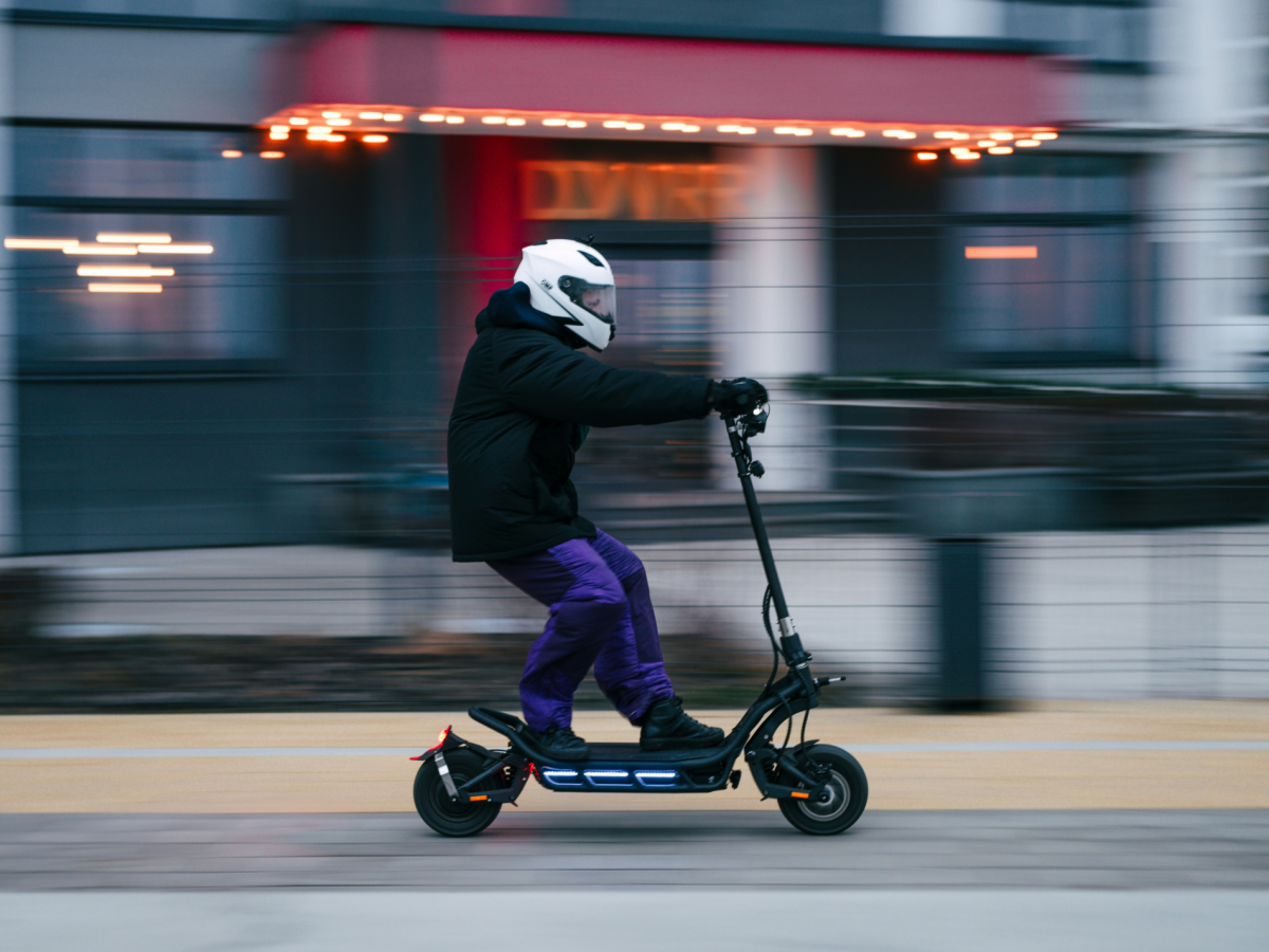 Person in winterlich warmer Kleidung und mit Motorradhelm auf dem Kopf fährt einen e-Roller.
