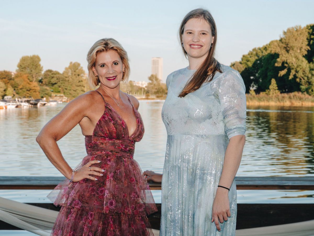Die beiden Frauen Alexandra Vetrovsky-Brychta, Präsidentin des DMVÖ, und Vivienne Nieuwenhuizen, neuen Geschäftsführerin des DMVÖ in festlicher Kleidung auf einem Halbportrait vor einem See fotografiert.
