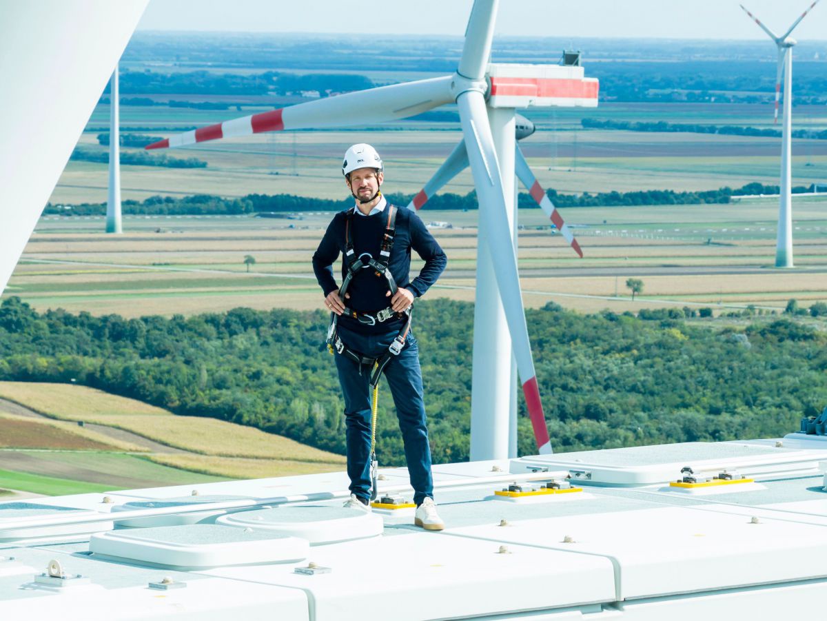 Lukas Püspök, Geschäftsführer des Energieunternehmens, steht auf einem Flügel eines Windrades. In luftiger Höhe. Im Hintergrund noch weitere Windräder in einer flachen Landschaft aus Feldern und Wäldern. 