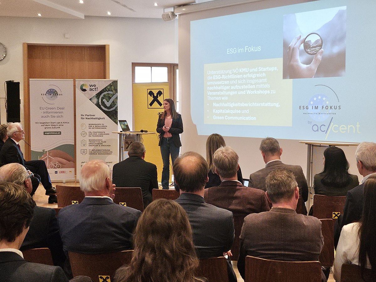 Publikum bei einem Vortrag, eine Frau in Hosenanzug steht am Pult und referiert.