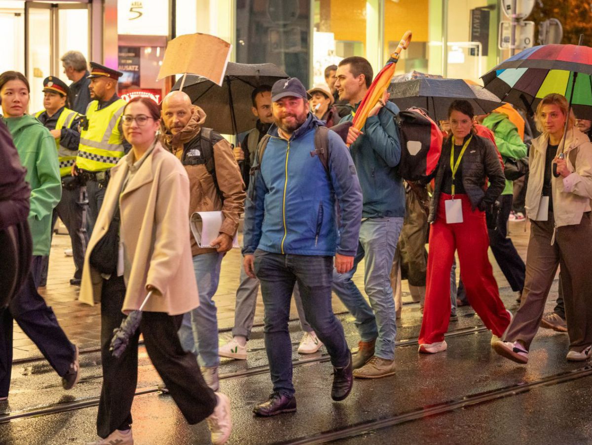 Eine Gruppe Menschen geht zu Fuß durch die Stadt, manche tragen Regenschirme.
