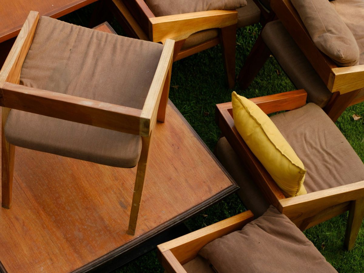 Designertische und Stühle aus Holz mit brauner Sitzauflage, teilweise übereinandergestapelt. Untergrund ist Wiese.