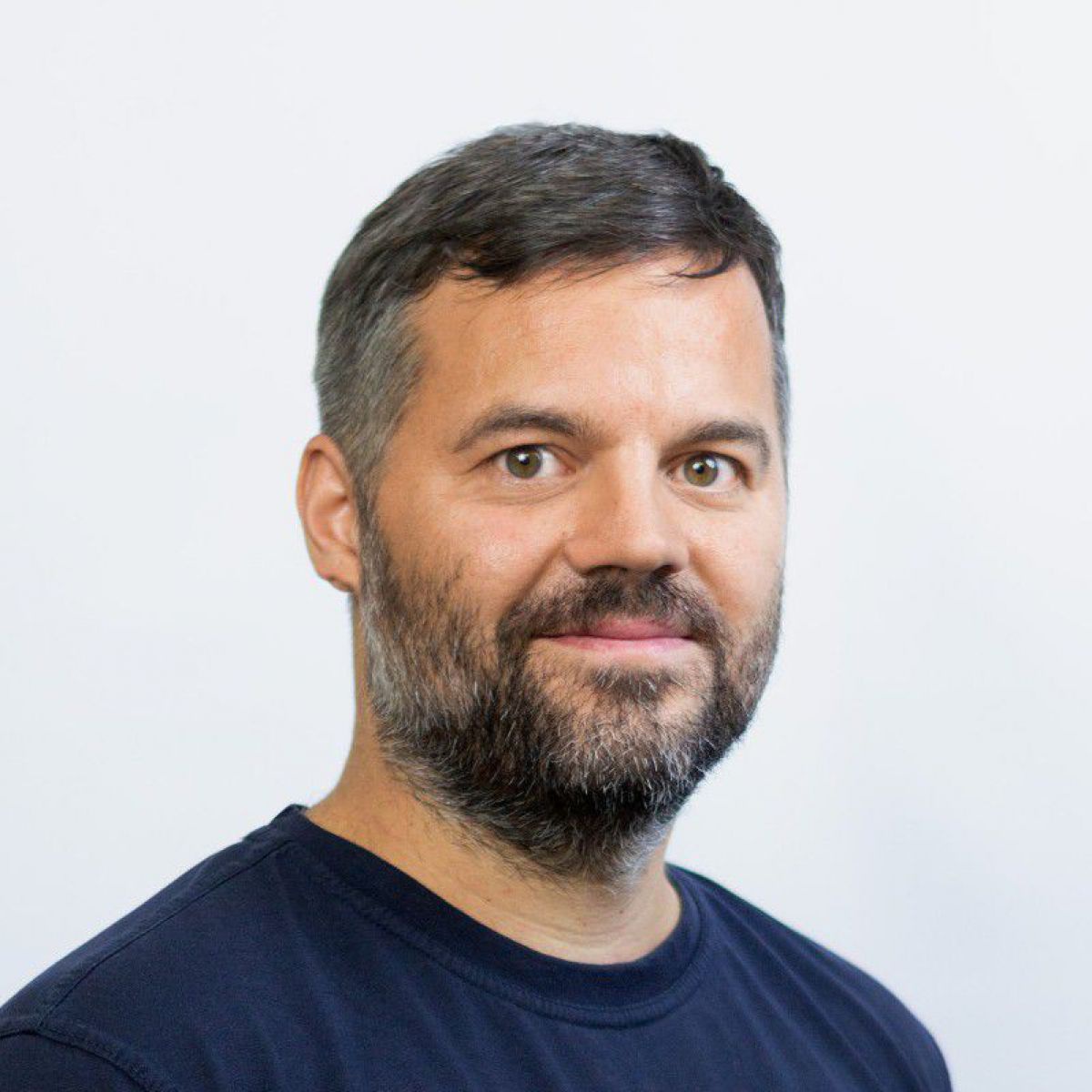Ein Mann mittleren Alters mit kurzen Haaren, Vollbart und freundlichen braunen Augen. Haar und Bart sind dunkel und schon etwas graumeliert. Er trägt ein dunkelblaues T-Shirt.