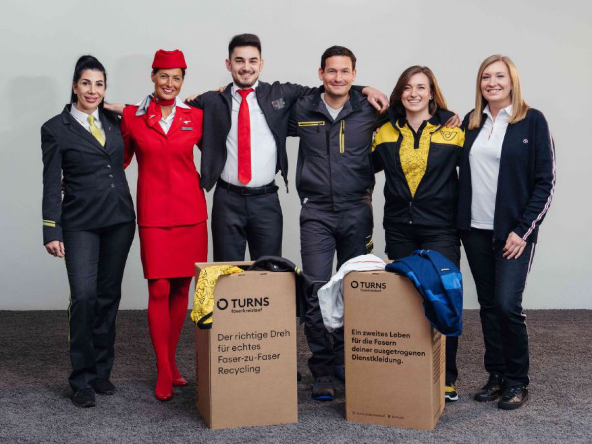 6 Personen, 4 Frauen und 2 Männer, posieren in Uniformen und Dienstkleidung der Post, Wiener Linien, Austrian Airlines, ÖBB, CAT und Salesianer Miettex. Vor ihnen stehen zwei Kartons, aus denen weitere Uniformstücke quellen.