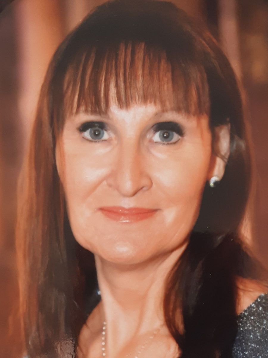 Portraitfoto von Sabine Krispel, eine Frau mittleren Alters mit schulterlangem braunen Haar und Stirnfransen, grünen Augen unter dunkel geschminkten Lidern.