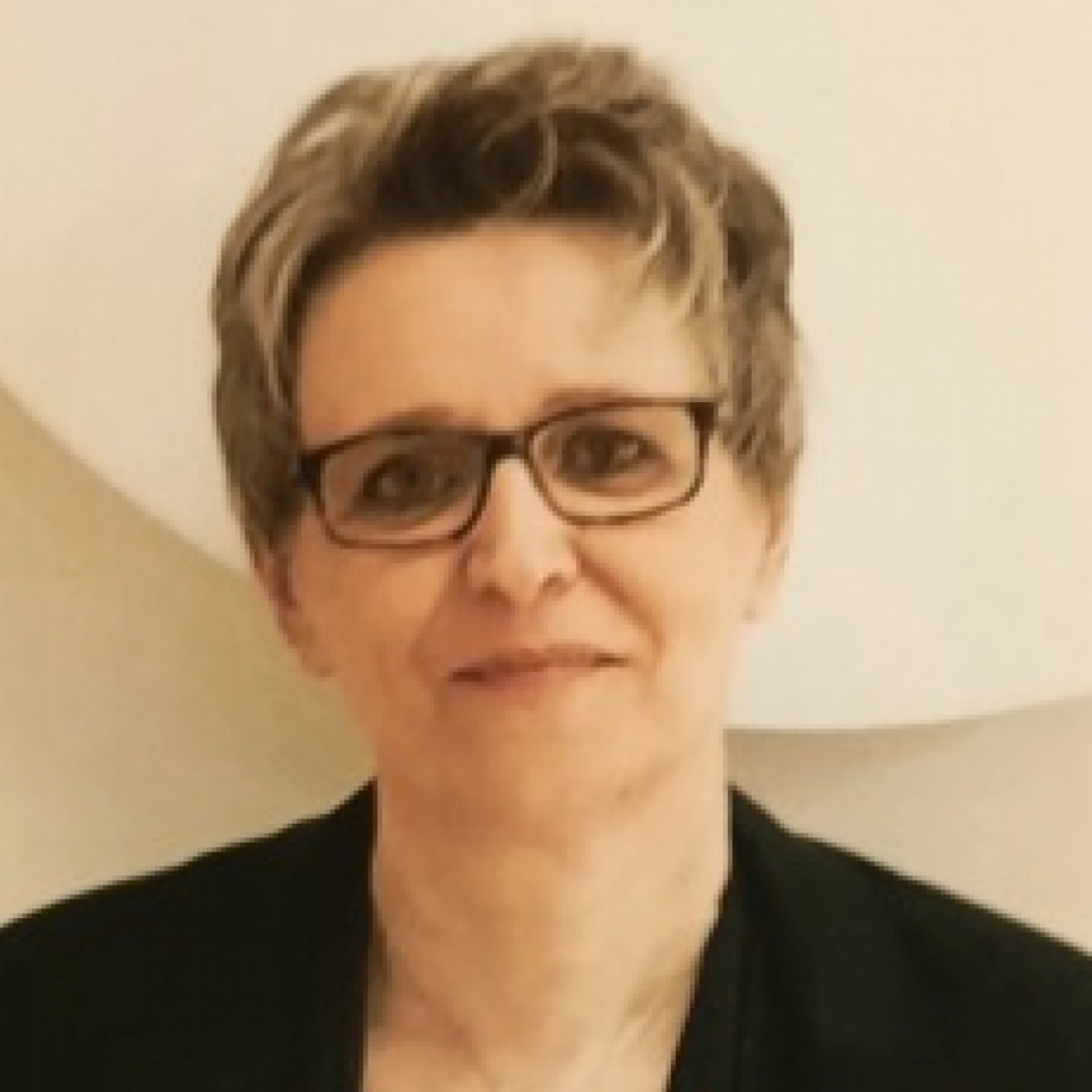 Portraitfoto von Dragana Serdar: Eine Frau mit blondem Kurzhaarschnitt und Brille im schwarzen Blazer vor weißem Hintergrund.