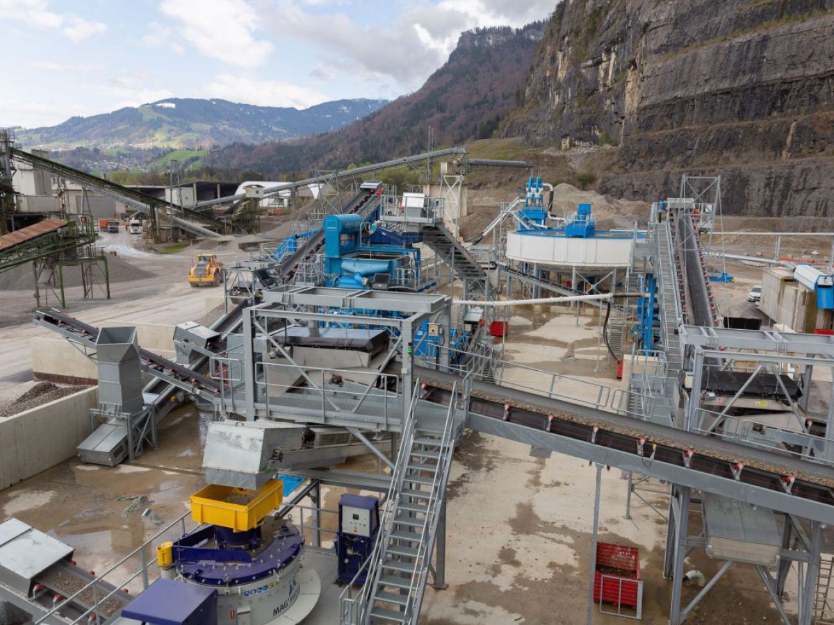 Blick von oben auf einen Teil der Recyclinganlage für Bodenaushubmaterial, welches auf einem riesigen Areal in gebirgiger Umgebung gelegen ist. Im Hintergrund sieht man steile Felswände mit Abtragungsspuren.