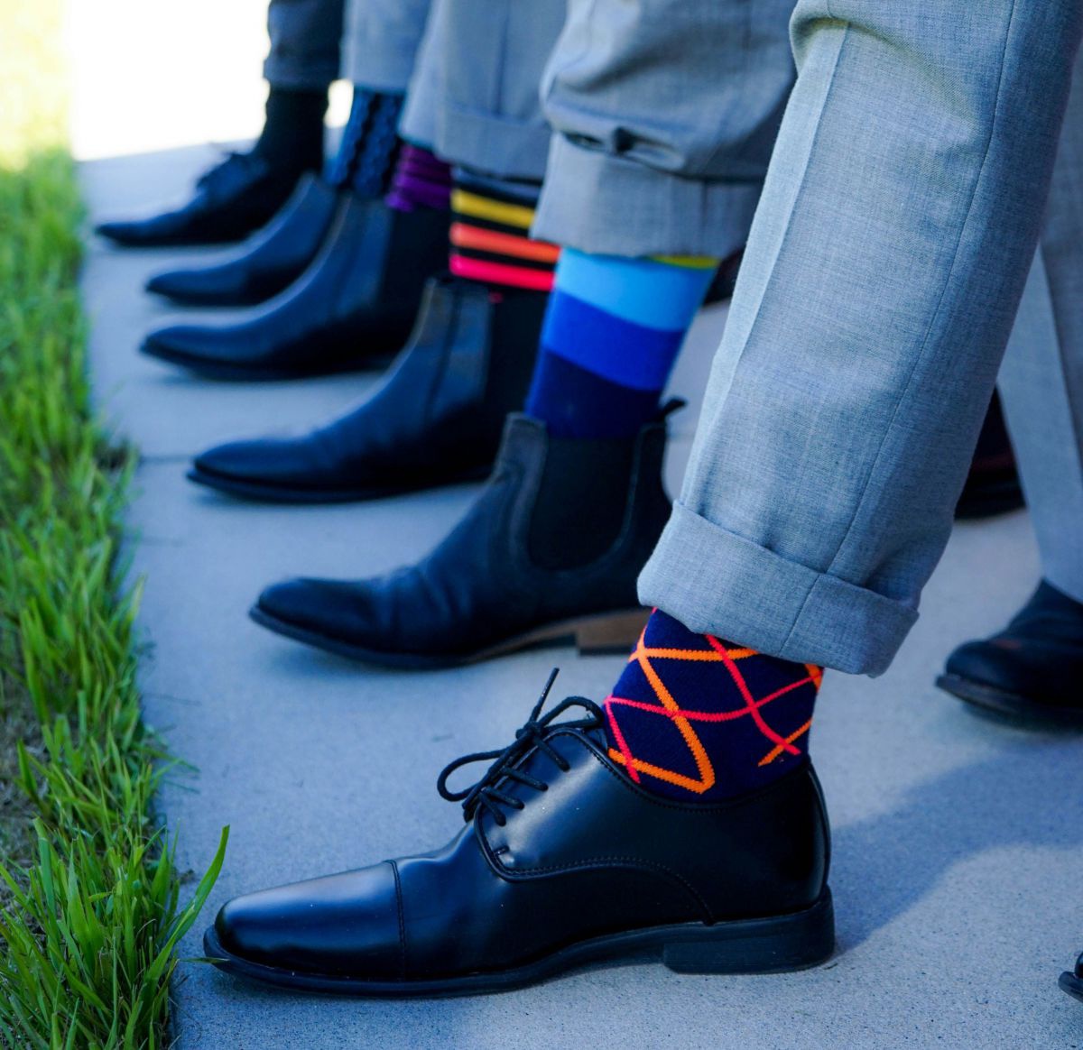 6 Männerbeine hintereinander bis zur Wade mit bunten Socken in schwarzen Businessschuhen.