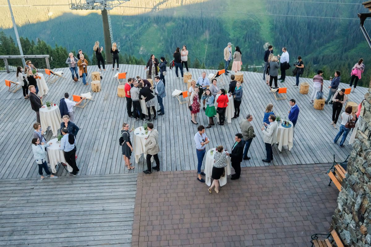 Vogelperspektive auf Menschengruppen an Stehtischen bei einem Event auf einer Dachterrasse.