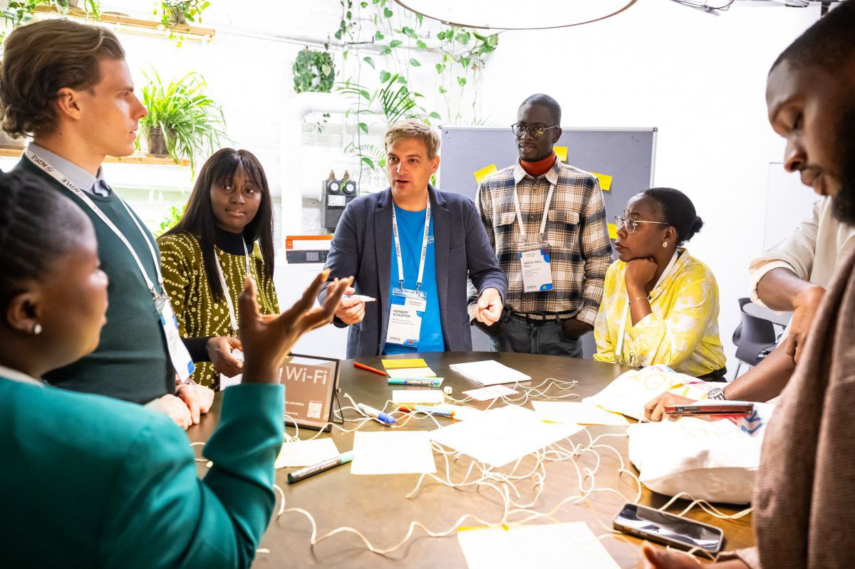 Eine Gruppe Männer und Frauen unterschiedlicher die rund um einen runden Tisch bei einem Führungskräftemeeting von Agile stehen und miteinander sprechen. 