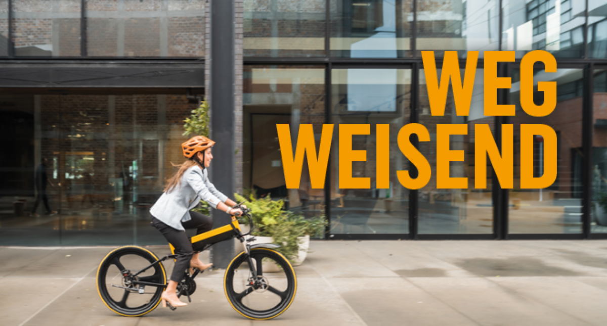 Eine Frau im Business-Kostüm, Stöckelschuhen und Fahrradhelm fährt mit dem Fahrrad an einem städtischen Gebäude mit Galsfronten vorbei. Titel: Wegweisend