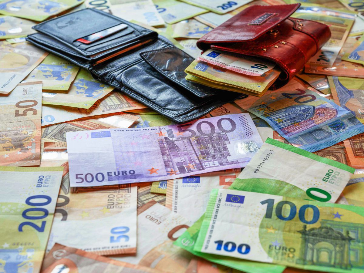 unzählige verschiedene Euro-Scheine liegen auf einem Tisch, darauf zwei geöffnete Geldbörsen - eine schlichte aus schwarzem Leder, eine aus braunem Leder mit Metallverzierungen.
