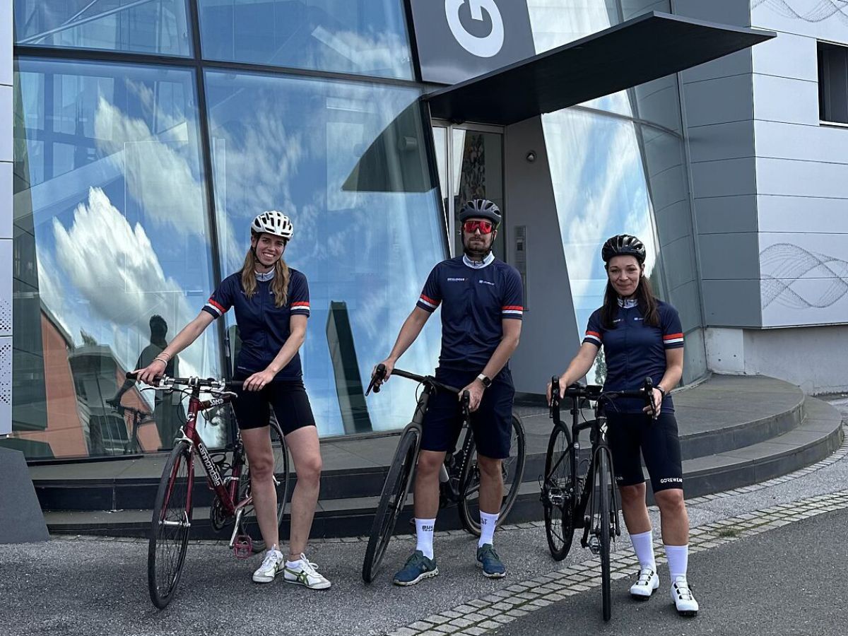 Drei Mitarbeiter*innen mit ihren Firmenrädern und ausgerüstet mit Fahrradkleidung und Helmen posieren vor dem Geschäftsgebäude von Geislinger.
