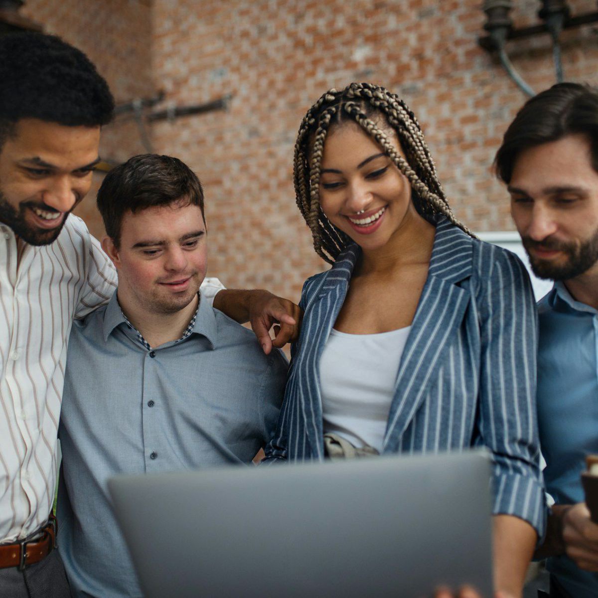 Ein Kolleg*innen-Team aus 4 Personen schaut sich gemeinsam mit interessierter Mimik und lächelnden Gesichtern etwas auf dem Bildschirm eines Laptops an.