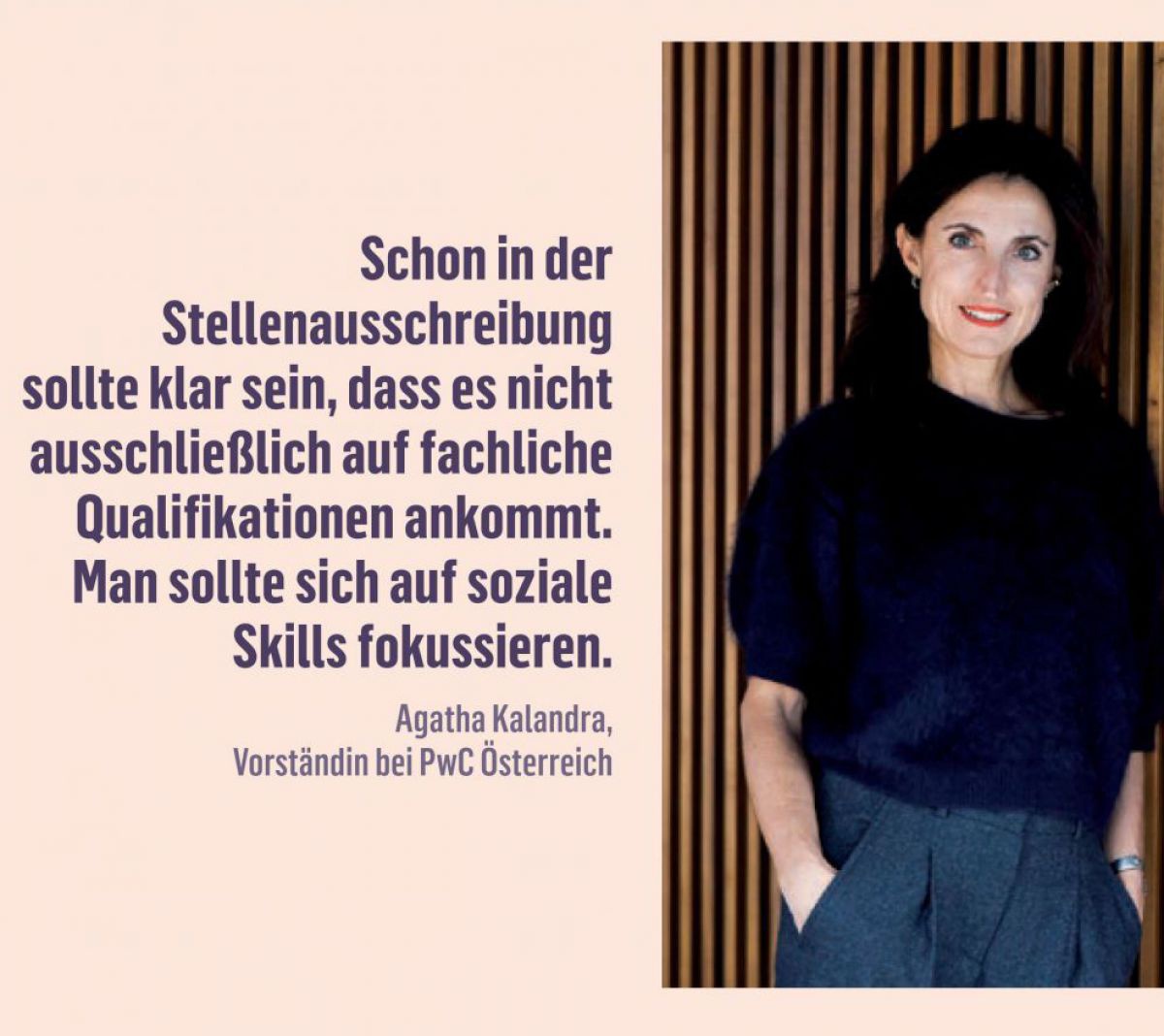Portraitfoto einer Frau mit dunklem langen Haar, das ihr offen über die Schultern fällt. Sie trägt eine graue Sakkohose, ein dunkelblaues Oberteil und lehnt, die Hände in den Hosensäcken, an einer Wand aus senkrechten, streifenförmigen Holzelementen.