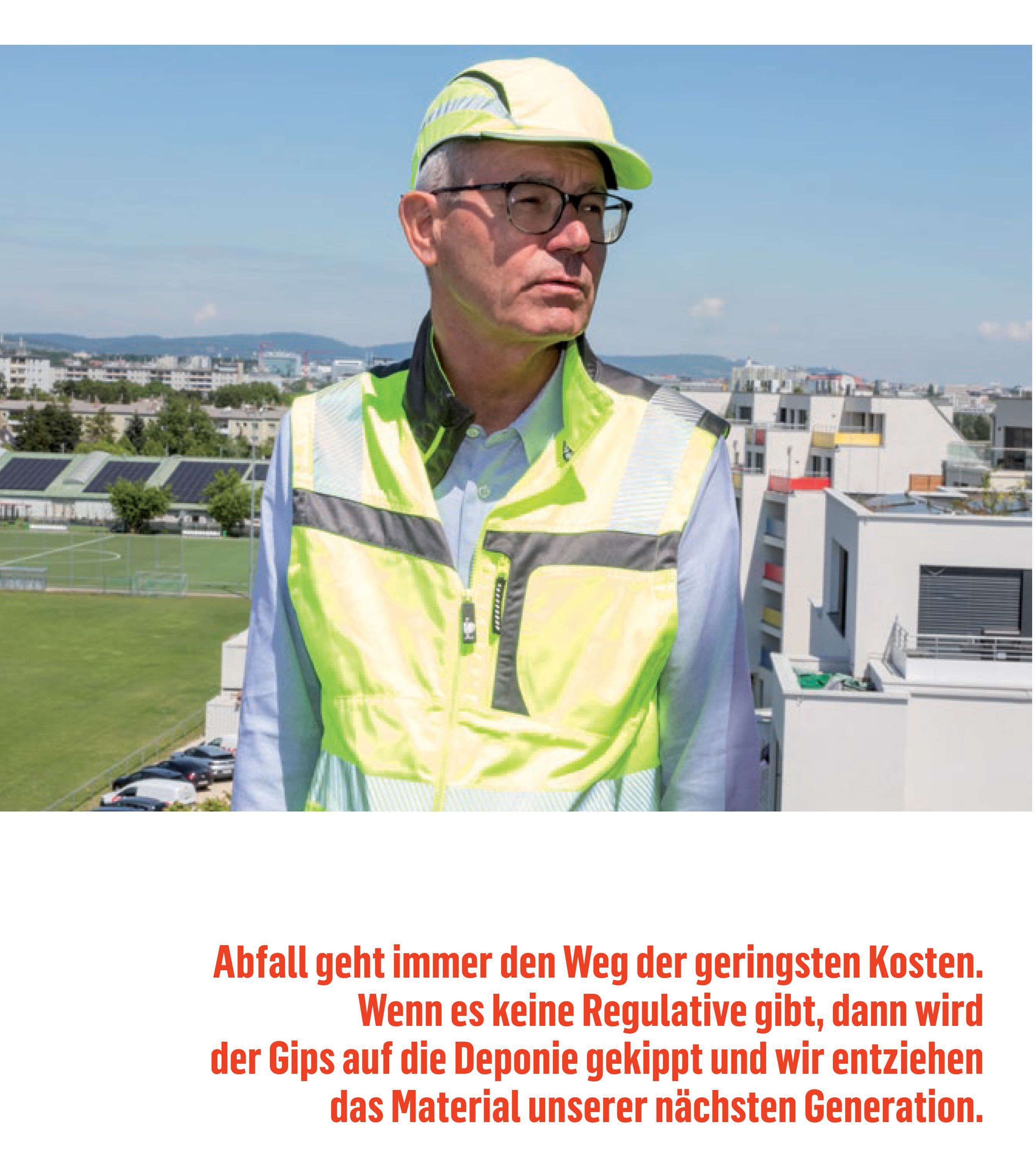Ein Mann in neon-gelber Sicherheitskleidung steht auf dem Dach eins Gebäudes und blickt in die Ferne, im Hintergrund sieht man die flachen Dächer weiterer Gebäude und die Rasenfläche eines Sportplatzes oder Parks.