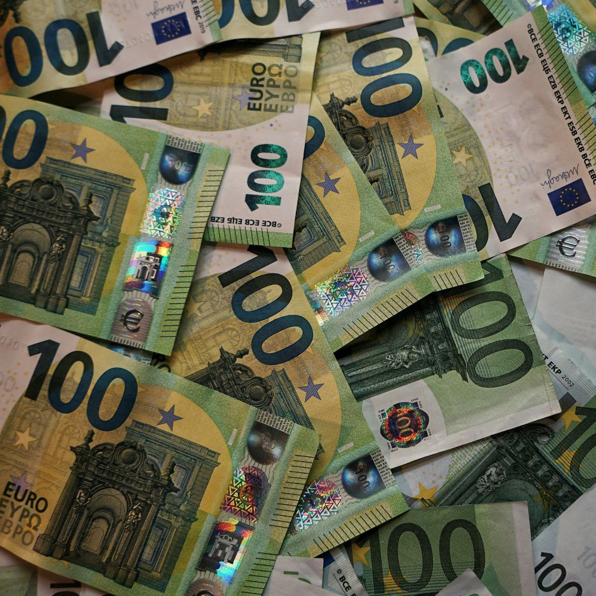Auf einer ebenen Fläche liegen viele 100-Euro-Scheine über- und untereinander, sodass man den Untergrund nicht sieht.
