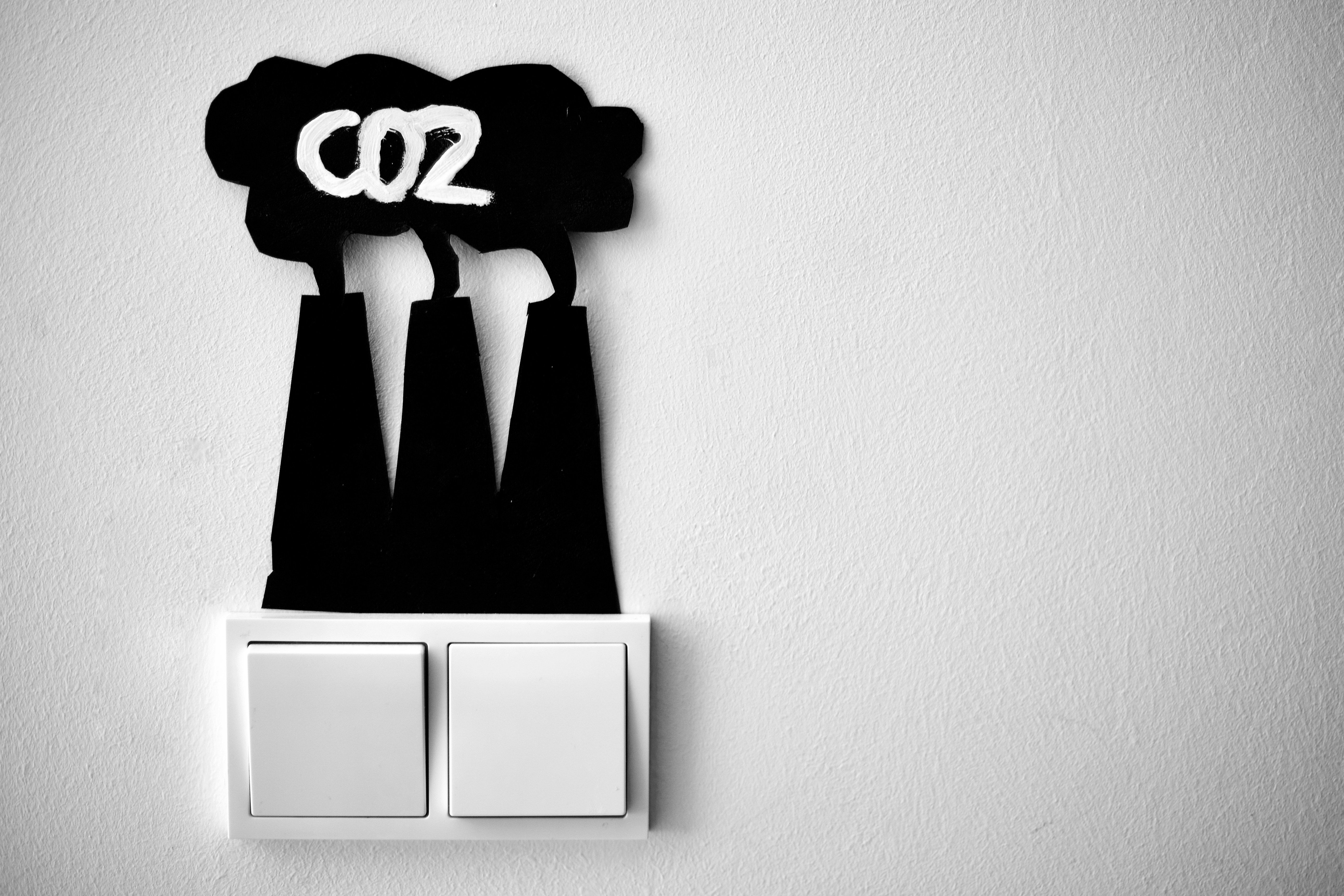 zwei Lichtschalter an einer weißen Wand, sie sind gegengleich gekippt und über ihnen ist ein Scherenschnitt aus schwarzem Karton angebracht, der drei Schornsteine mit Wolken darüber darstellt, darin steht in weißer Schrift 