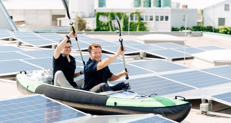 Die Geschäftsführer Adam Gözsy und Marc Falle paddeln scheinbar im Schlauchboot inmitten der Solarpanele. Foto: Tausendundein Dach