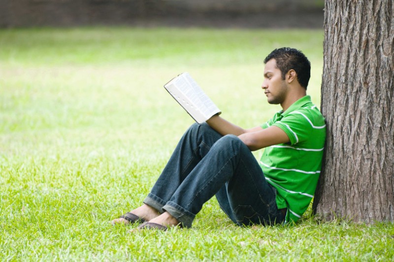 Ein Mann lehnt an einem Baumstamm und liest ein Buch