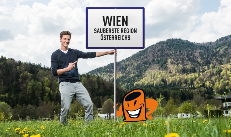 Ein junger Mann steht in einer Wiese und hält ein Schild mit dem Aufdruck "Wien ist die sauberste Region Österreichs 2017".