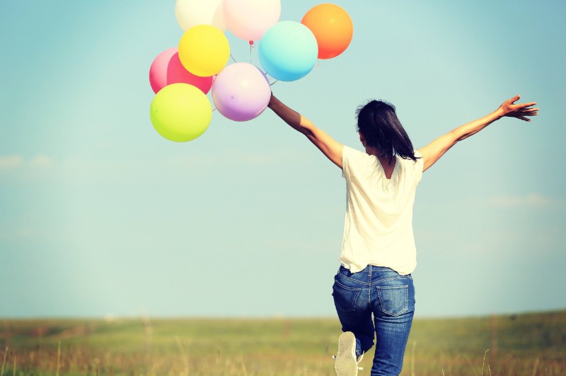 Eine junge Dame läuft mit Luftballons in der Hand über eine Wiese