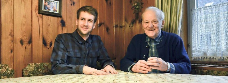 Wohnbuddies. Ein Student und ein älterer Mann sitzen am Tisch und lachen in die Kamera.. Foto: Wohnbuddy