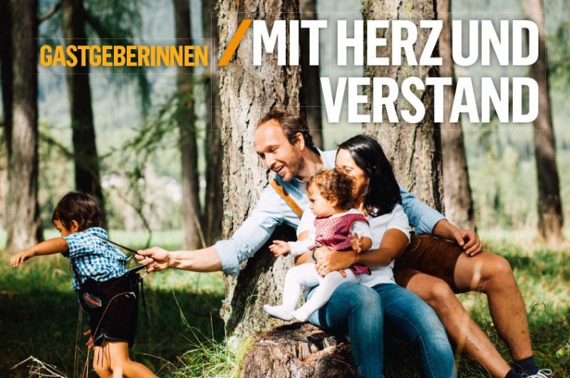 Die Familie Föger sitzt auf einem Baumstamm im Wald. Der kleine Sohn will auf und davon. Der Vater hält ihn am Hosenträger.