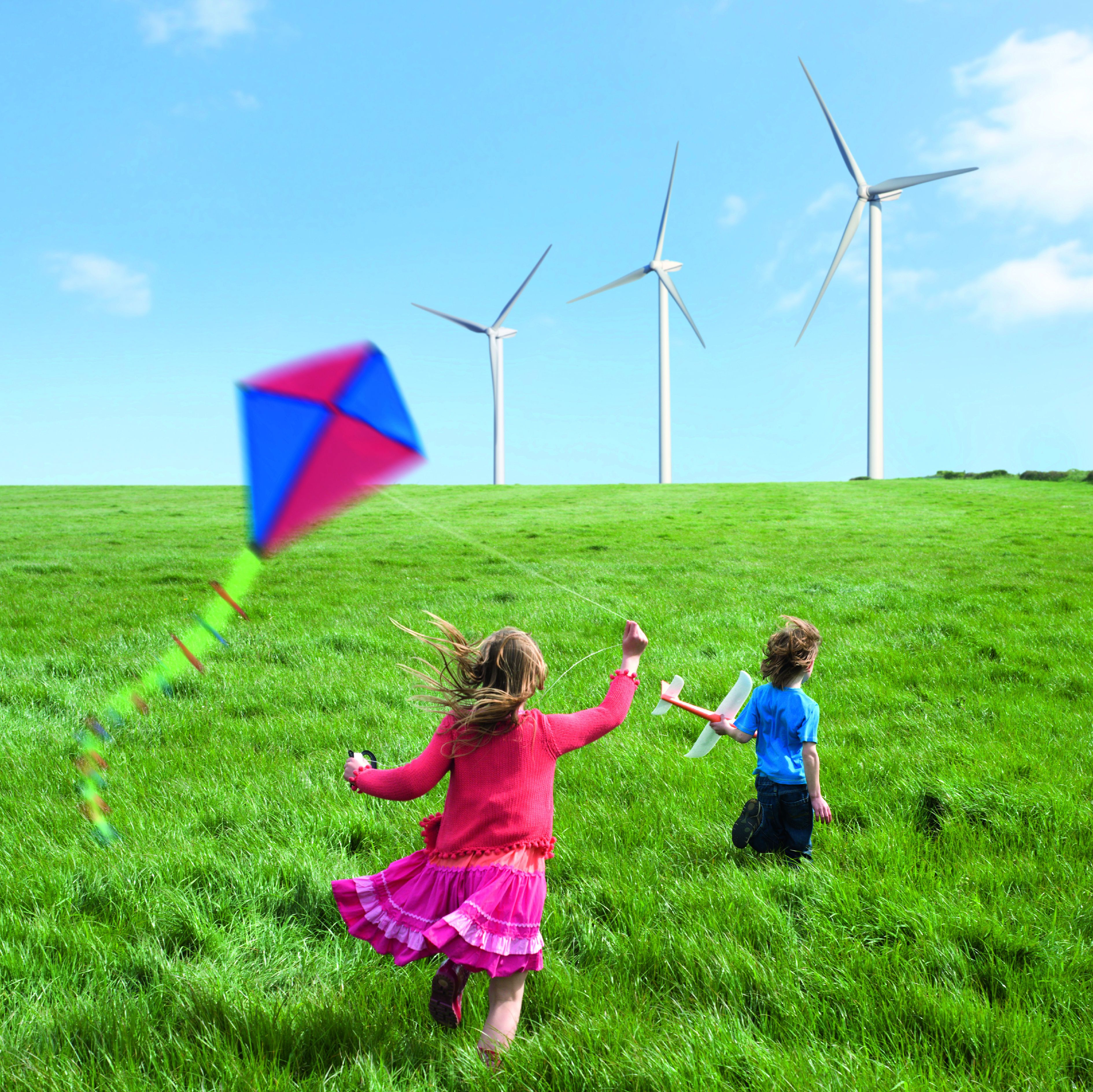 Kinder lassen Drachen steigen, grüne Wiese, Windräder im Hintergrund