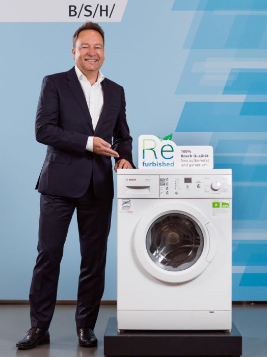 Michael Mehnert, CEO der BSH Österreich präsentiert stolz eine professionell wiederaufbereitete Waschmaschine.