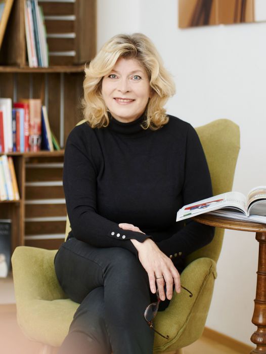 Doris Palz sitzt vor einem Bücherregal in einem hellgrünen Lehnstuhl.