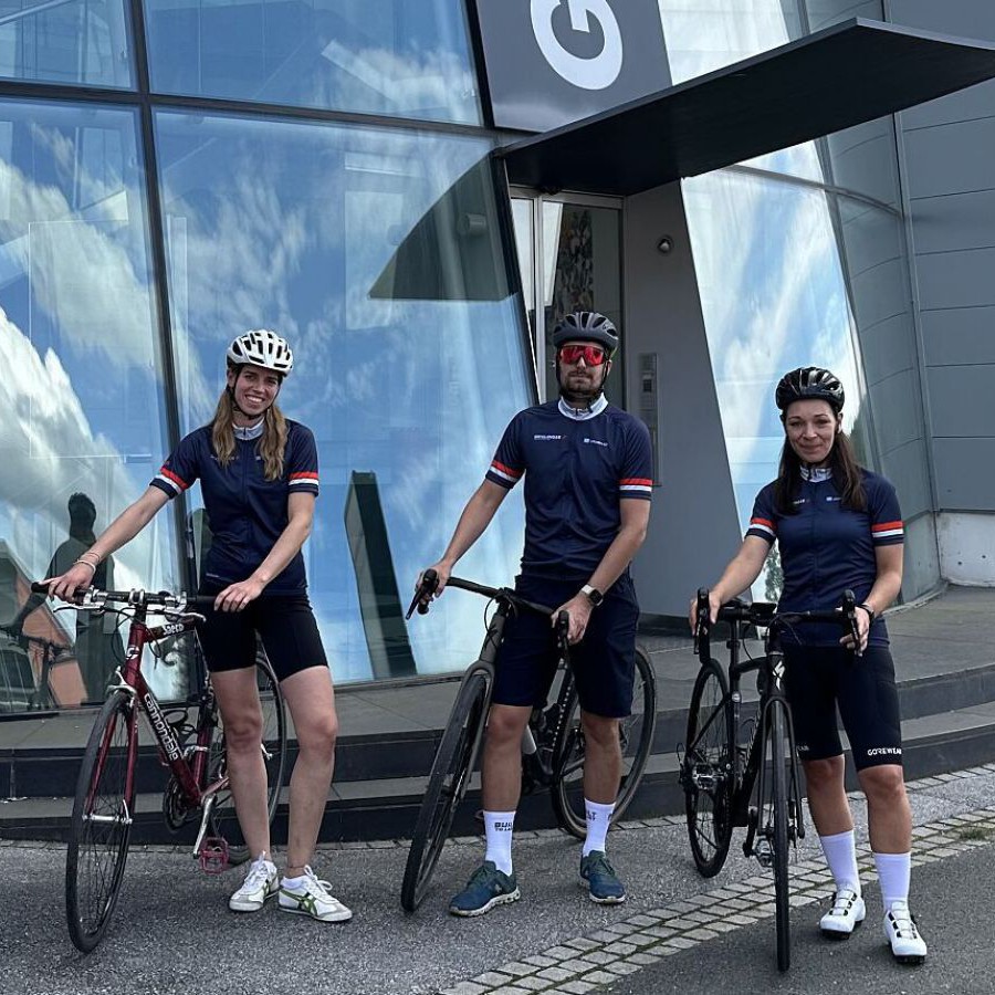 Drei Mitarbeiter*innen mit ihren Firmenrädern und ausgerüstet mit Fahrradkleidung und Helmen posieren vor dem Geschäftsgebäude von Geislinger.