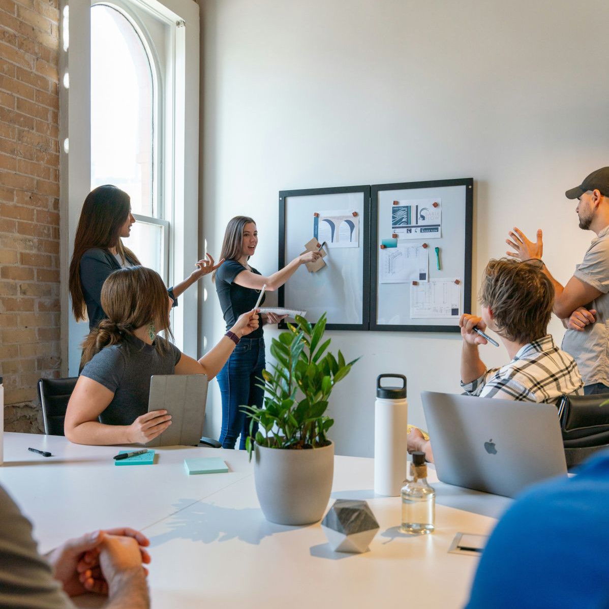 Frauen und Männer, die auf ein Whiteboard schauen, wo dem Grafiken sind, die eine Person erklärt, ein Symbolfoto für Führung